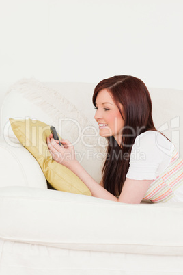 Gorgeous red-haired female writing a text on her phone while lyi