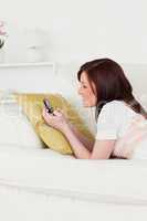 Cute red-haired female writing a text on her phone while lying o