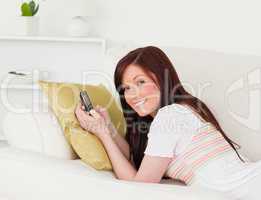 Joyful red-haired female writing a text on her phone while lying