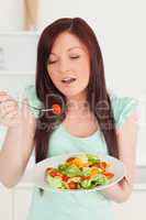 Young red-haired woman enjoying a mixed salad in the kitchen