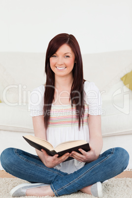 Good looking red-haired woman reading a book while sitting on a