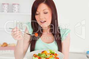 Charming red-haired woman enjoying a mixed salad in the kitchen