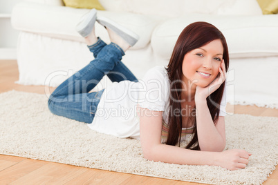 Smiling red-haired woman posing while lying on a carpet