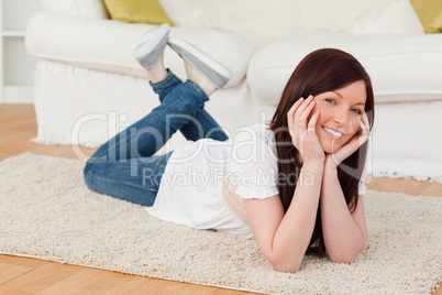 Beautiful red-haired woman posing while lying on a carpet