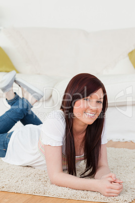Good looking red-haired woman posing while lying on a carpet