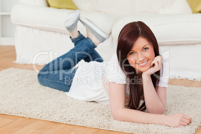 Attractive red-haired woman posing while lying on a carpet