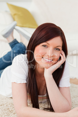 Joyful red-haired woman posing while lying on a carpet
