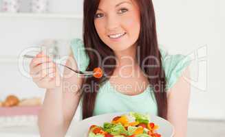 Cute red-haired woman enjoying a mixed salad in the kitchen