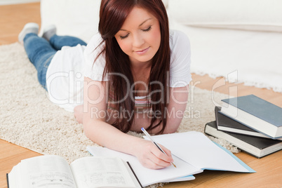 Beautiful joyful red-haired girl studying for while lying on a c