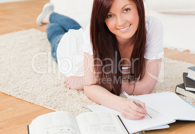 Attractive red-haired girl studying for while lying on a carpet