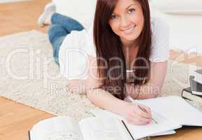 Attractive red-haired girl studying for while lying on a carpet