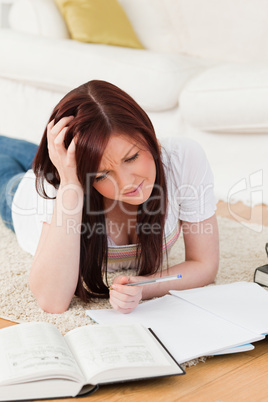 Pretty red-haired girl studying for while lying on a carpet