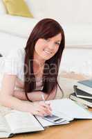 Attractive red-haired female studying for while lying on a carpe