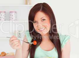 Pretty red-haired woman cutting eating a cherry tomato in the ki
