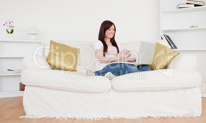 Attractive female sitting on a sofa is going to make a payment o