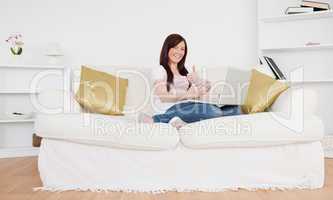 Pretty female sitting on a sofa is going to make a payment on th