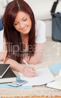 Cute red-haired female studying for while lying on a carpet