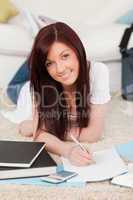 Gorgeous red-haired female studying for while lying on a carpet