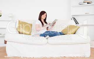 Attractive red-haired female relaxing with her tablet while sitt