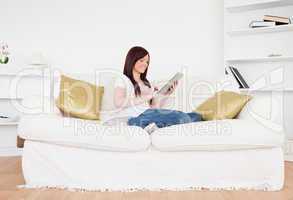 Beautiful red-haired female relaxing with her tablet while sitti