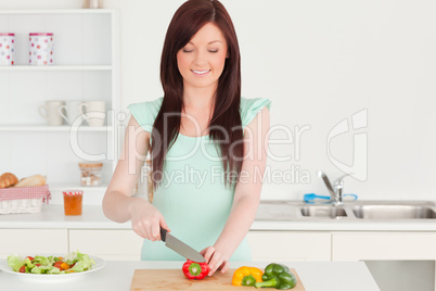 Attractive red-haired woman cutting some vegetables in the kitch