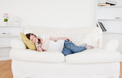 Beautiful red-haired female watching tv while lying on a sofa