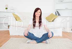Beautiful red-haired female posing while sitting on a carpet