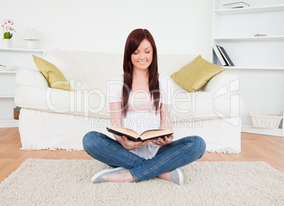 Beautiful red-haired female reading a book while sitting on a so