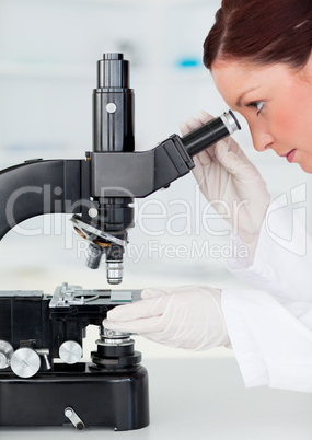 Beautiful red-haired scientist looking through a microscope