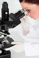 Pretty red-haired scientist looking through a microscope