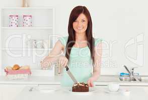 Attractive red-haired woman cutting some cake in the kitchen