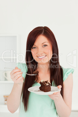 Pretty red-haired woman eating some cake in the kitchen