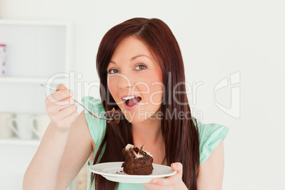 Charming red-haired woman eating some cake in the kitchen