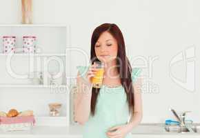 Attractive red-haired woman enjoying a glass of orange juice in