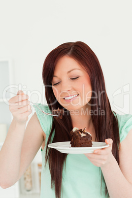 Joyful red-haired woman eating some cake in the kitchen