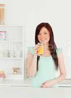 Joyful red-haired woman enjoying a glass of orange juice in the