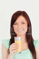 Cheerful red-haired woman enjoying a glass of orange juice in th