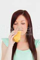 Attractive red-haired woman drinking a glass of orange juice in