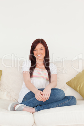 Attractive red-haired woman posing while sitting on a sofa in th