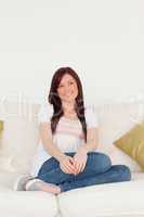 Smiling red-haired woman posing while sitting on a sofa