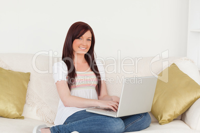 Attractive red-haired woman relaxing with her laptop while sitti