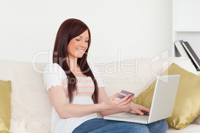 Good looking woman sitting on a sofa is going to make a payment