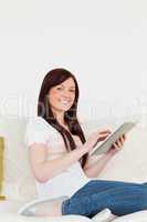 Attractive red-haired woman relaxing with her tablet while sitti