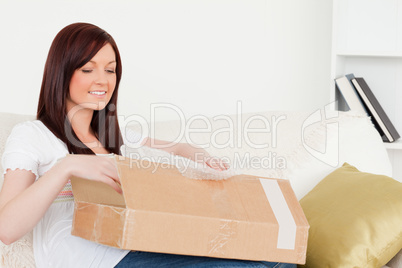 Attractive red-haired woman opening a carboard box while sitting