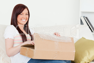 Beautiful red-haired woman opening a carboard box while sitting