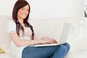 Pretty red-haired woman relaxing with her laptop while sitting o