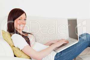 Beautiful red-haired woman relaxing with her laptop while lying