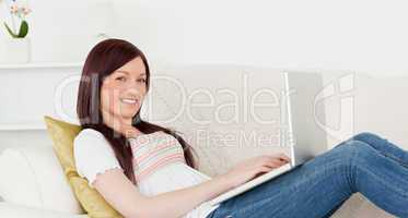 Attractive red-haired woman relaxing with her laptop while lying