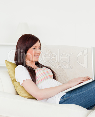 Charming red-haired woman relaxing with her laptop while lying o