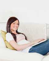 Cute red-haired woman relaxing with her laptop while lying on a